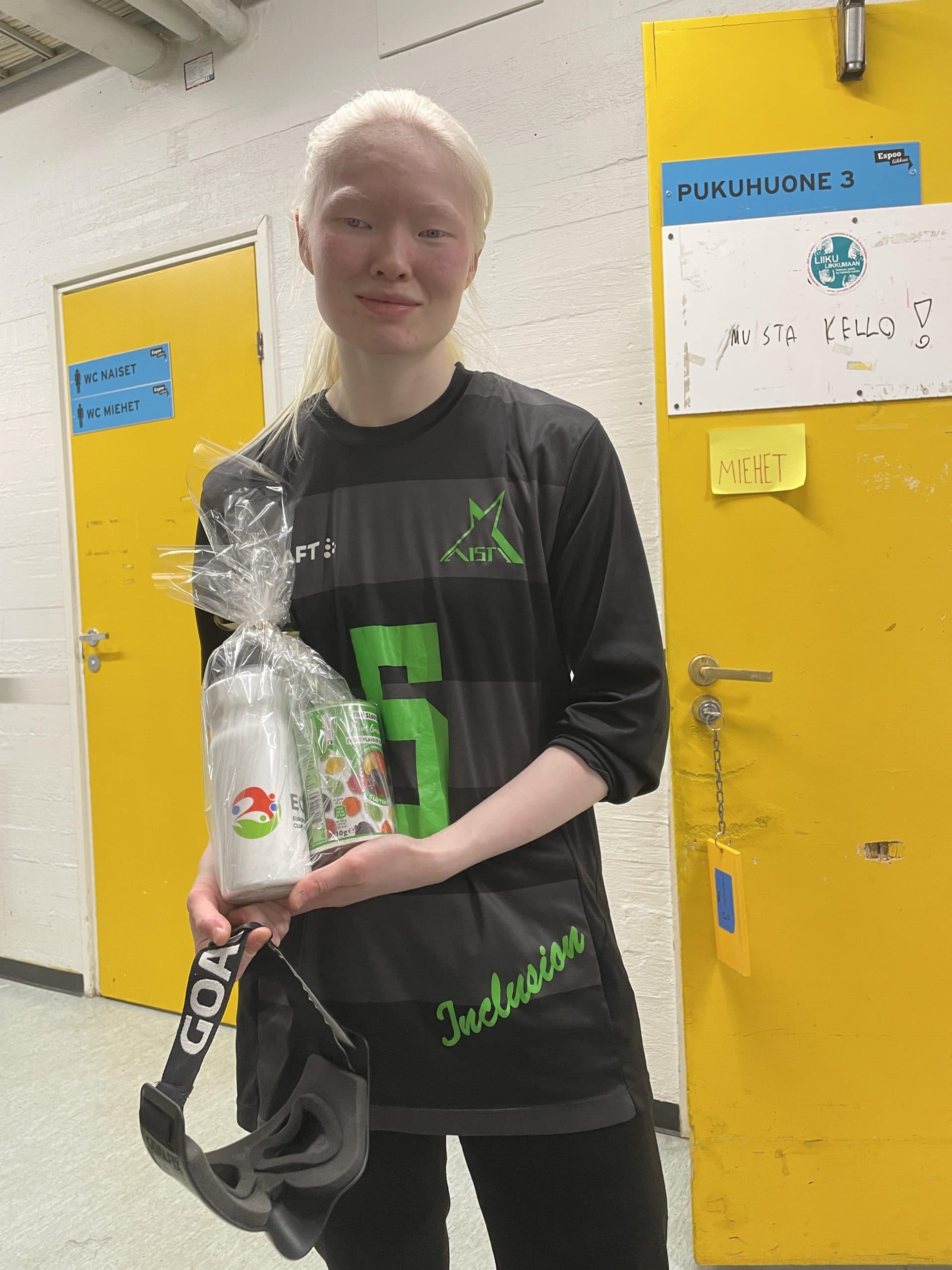 Rebekah poseeraamassa parhaan puolustajan palkinnon kanssa pukuhuonekäytävällä pelivarusteissa.
