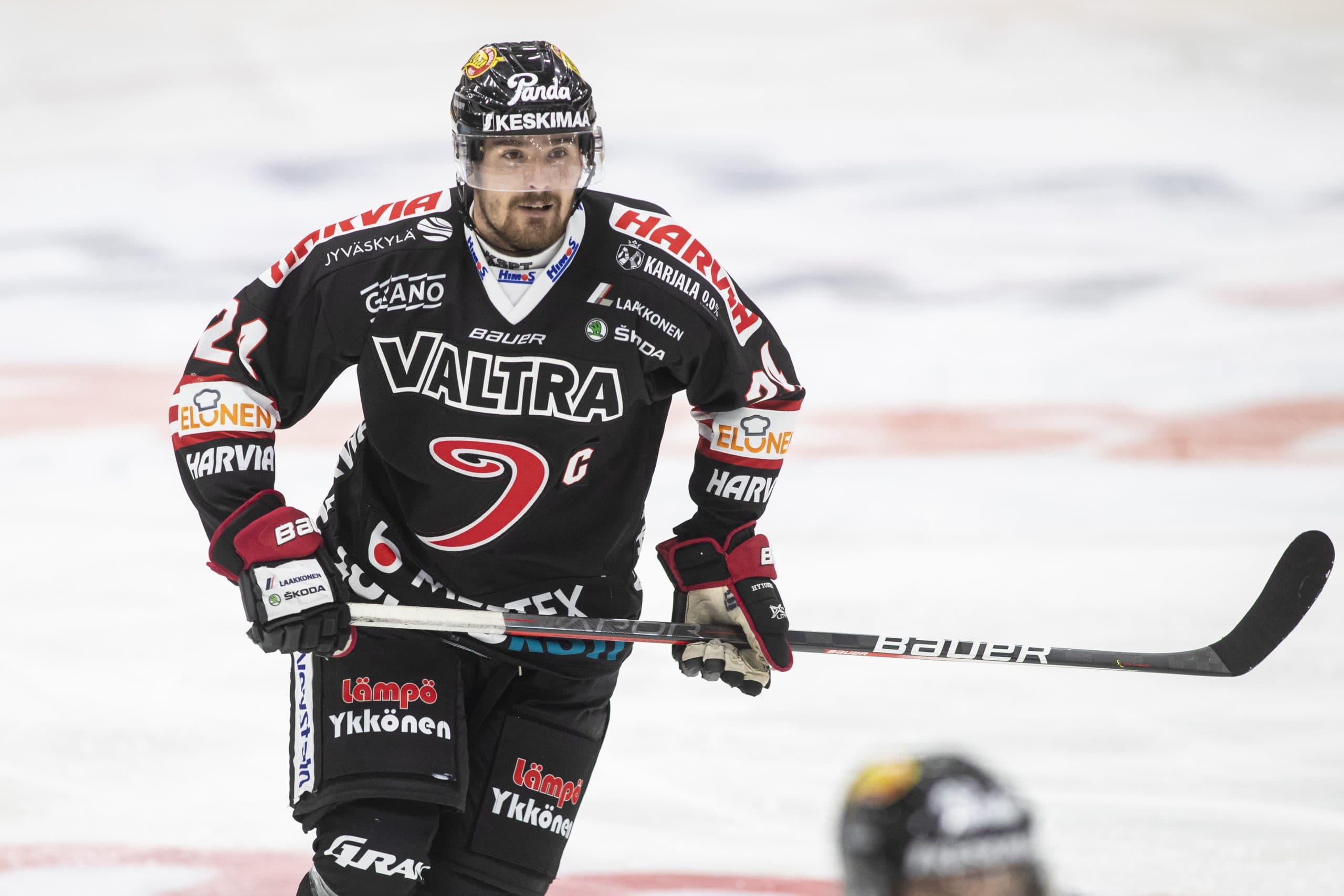 Kuva jäältä jossa Jypin pelaaja luistelee kameraa kohti Jypin mustissa kotiväreissä.