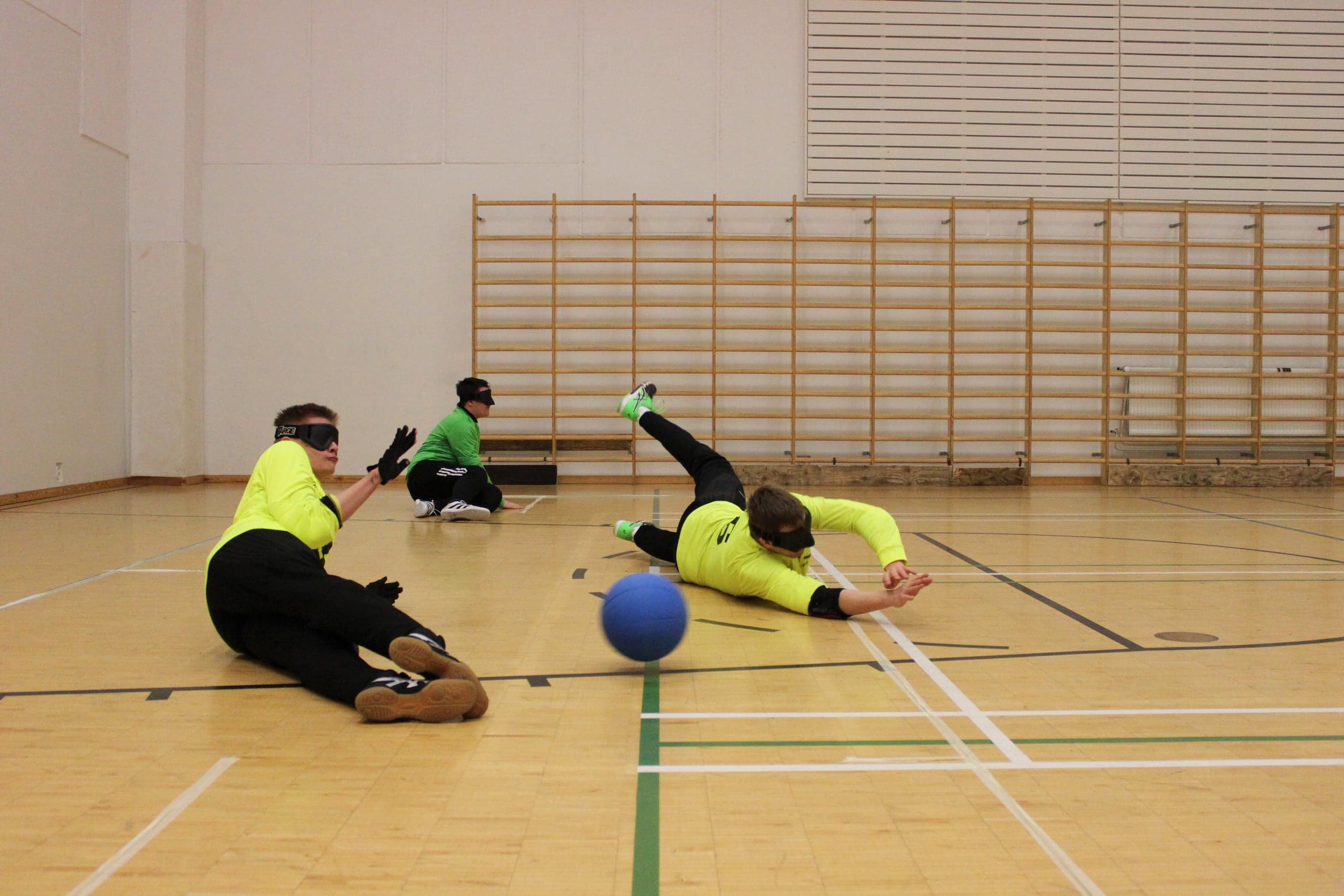 An action shot where two players in flumino jerseys and one in a green jersey block the ball.