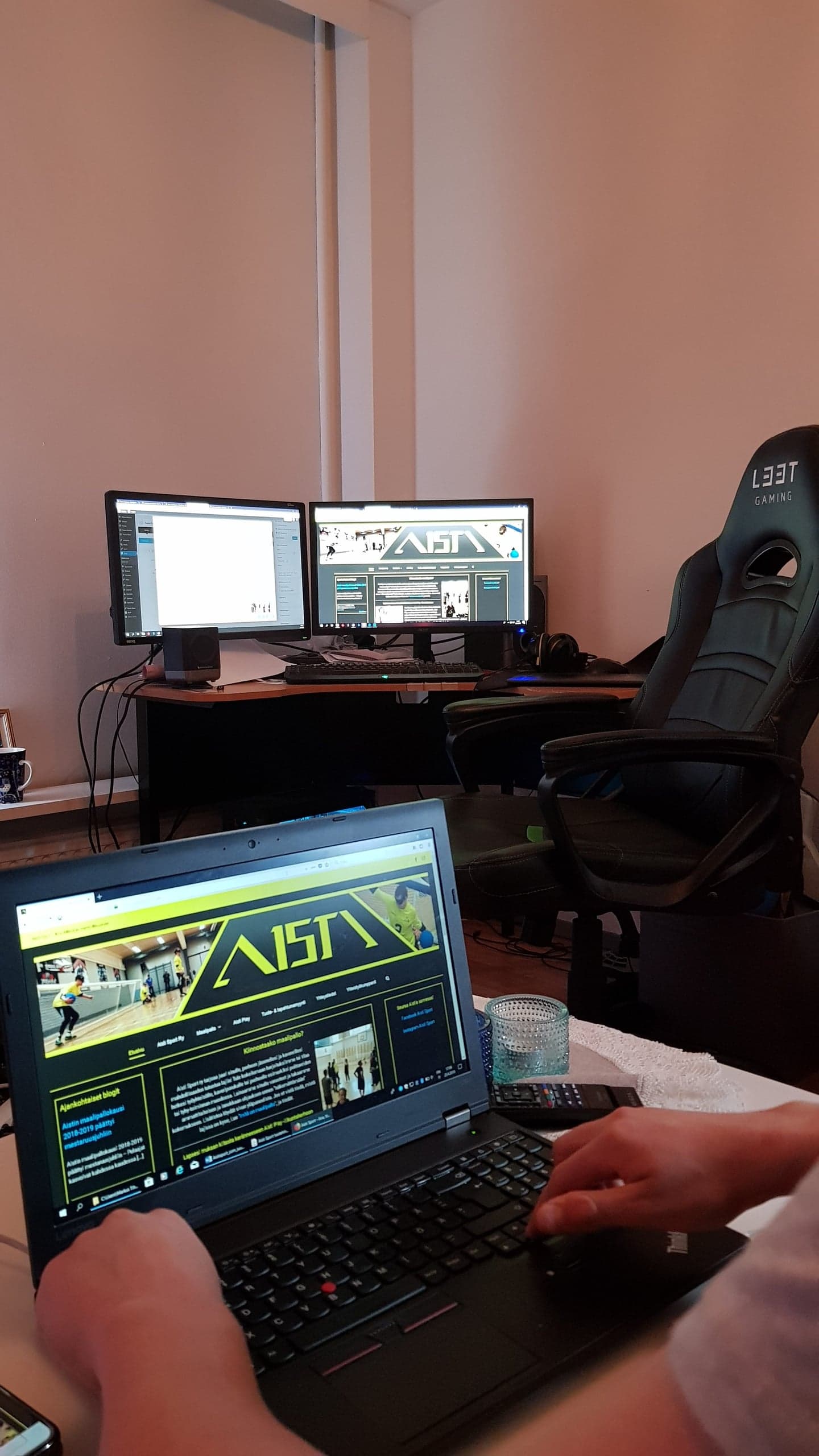 A photo with Markus's hands in the foreground on a laptop running JAWS, and two screens running on Samuli's computer. Every display is working on the aistisport.com website.