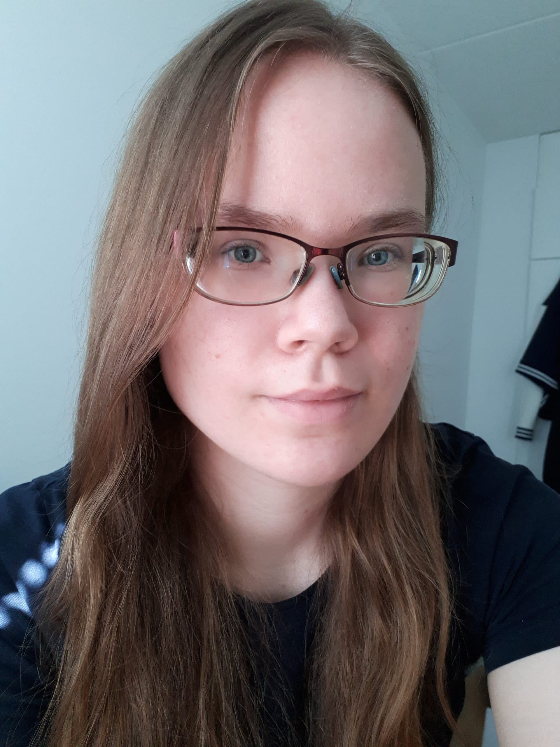 Hymyilevä kasvokuva Miinasta; ruskeat hiukset, silmälasit ja tumma t-paita.