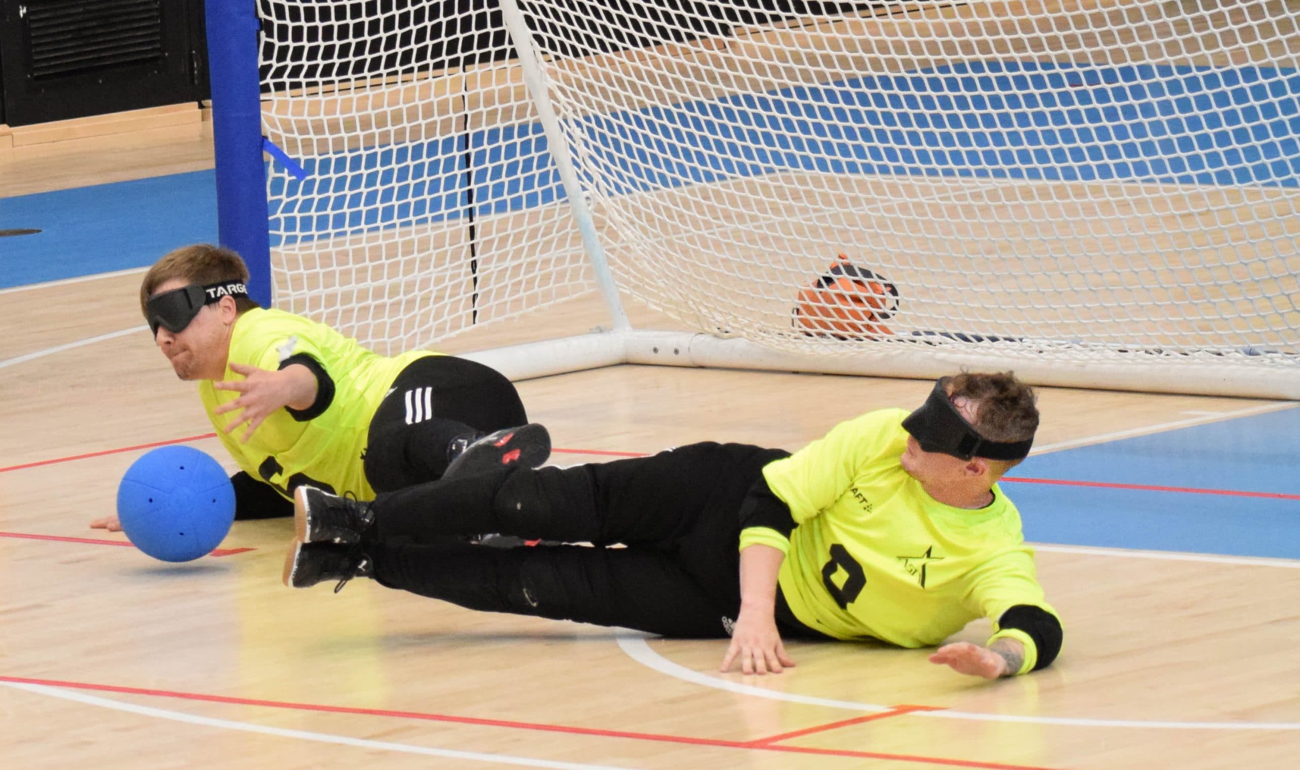 Pelitilannekuva torjuntatilanteesta jossa Aisti Sportin fluminokeltaisissa paidoissa olevat sentteri ja laituri syöksyvät torjumaan lähestyvää palloa.