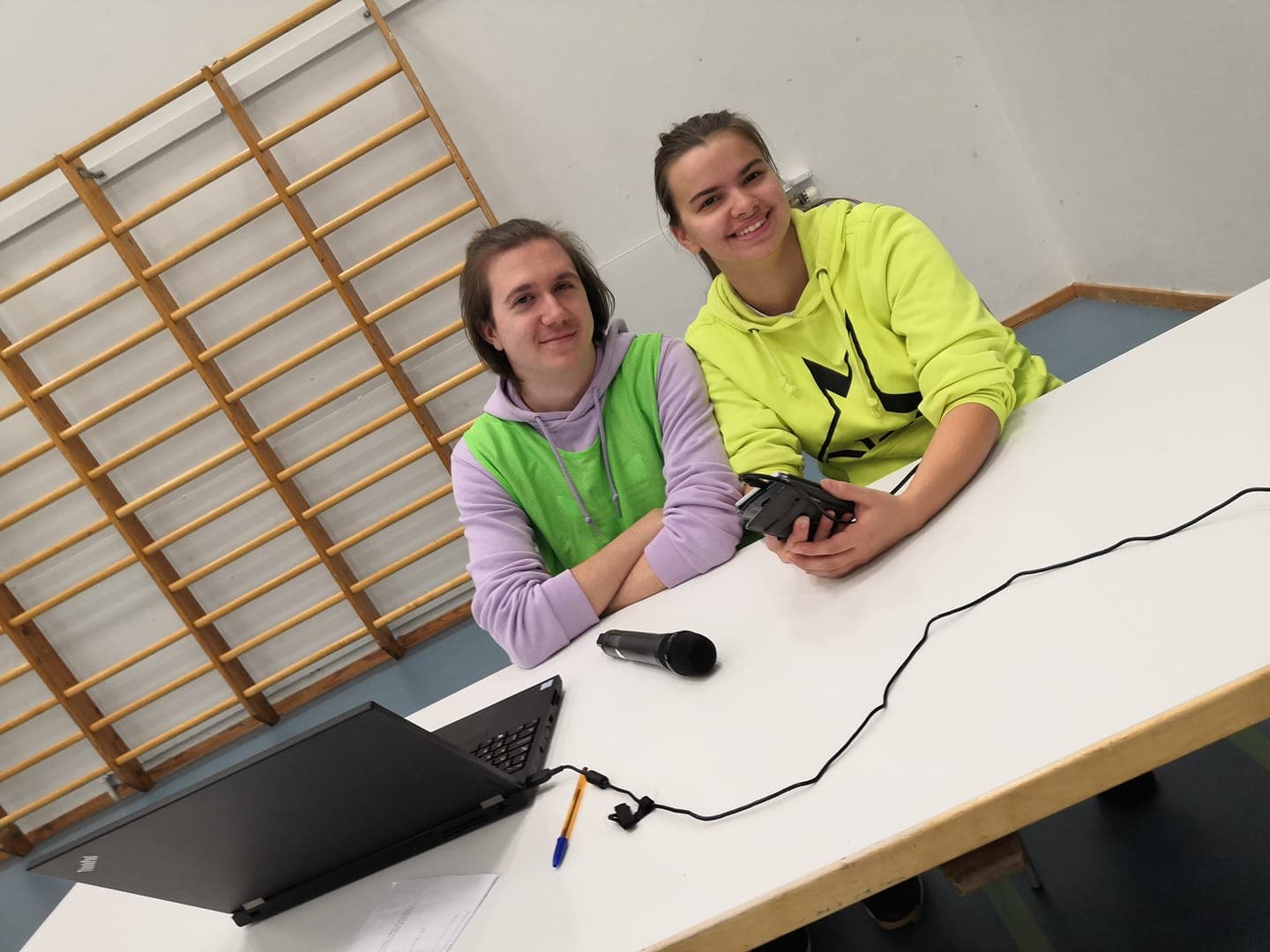 TJ-pöydän luona hymyilevä nuori nainen ja nuori mies toimitsijan tehtävissä