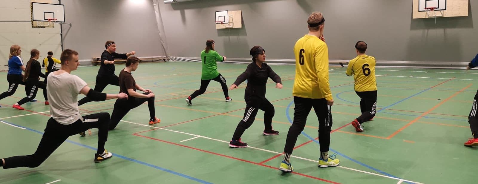 Tilannekuva harjoituksista, jossa 11 harrastajaa askelkyykky asennossa kädet sivuilla tekemässä alkulämmittelyä