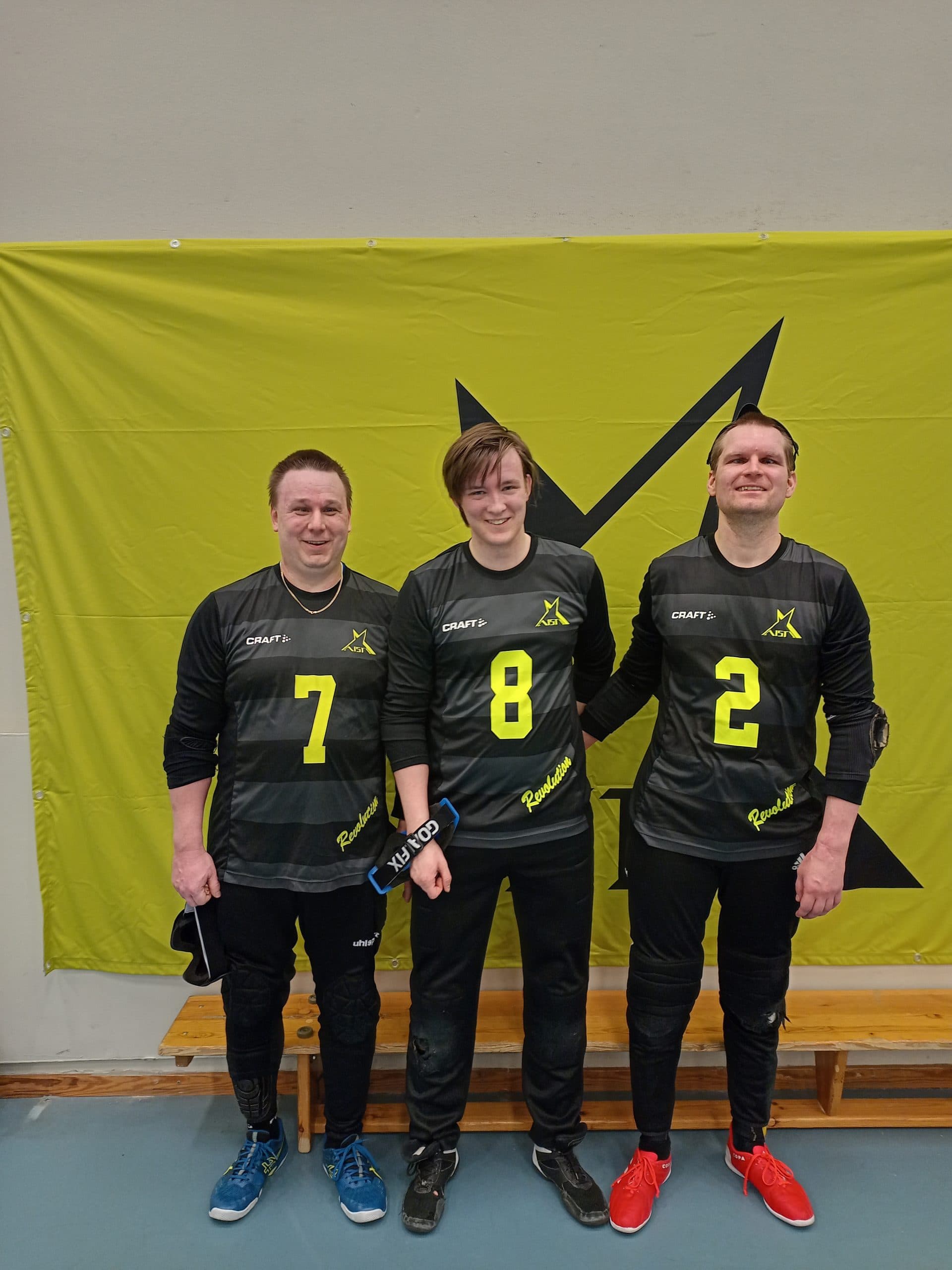A smiling team photo of Petri, Leo and Ville in front of an Aisti banner.