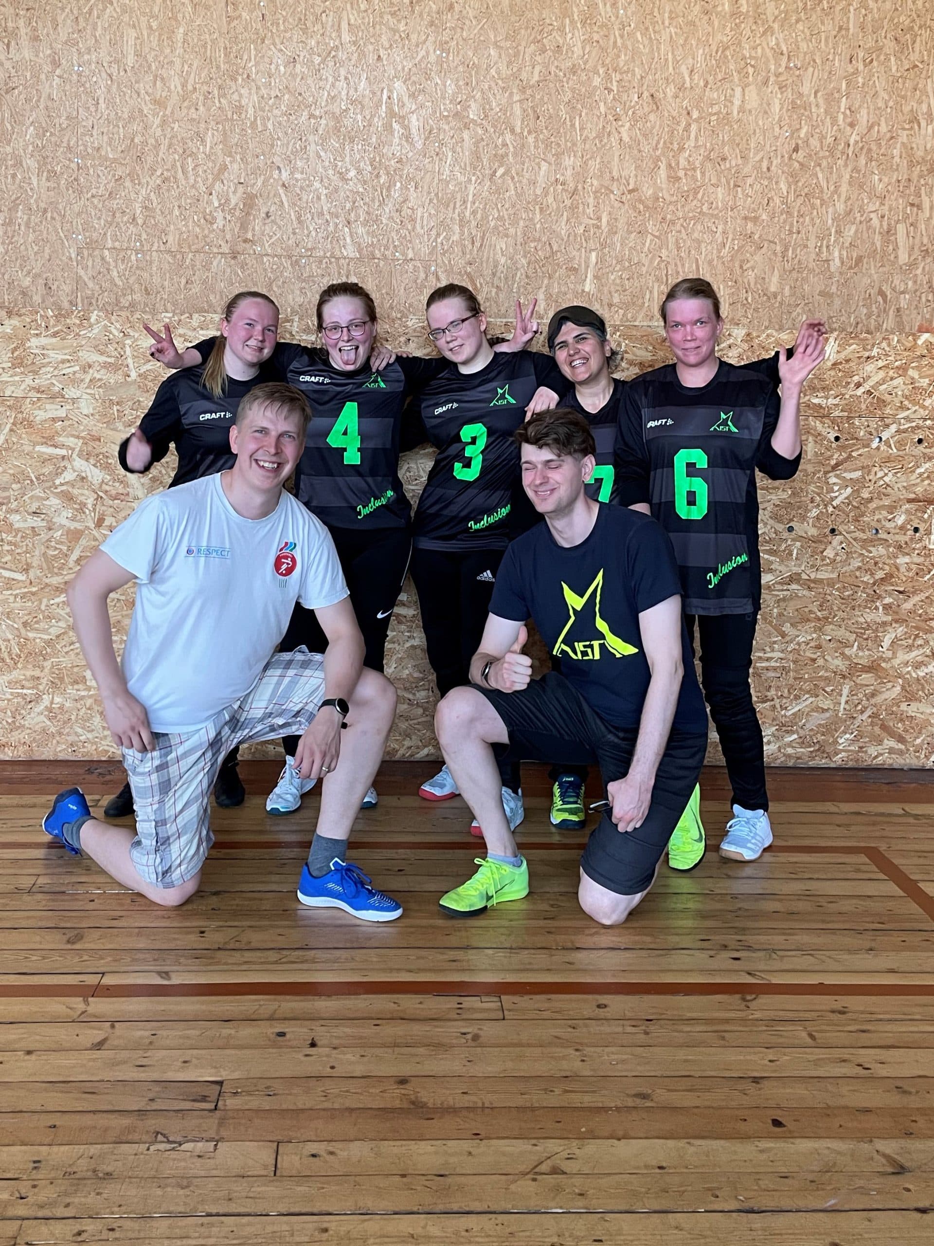 A sweaty group photo of the team after a won game. Back row, from left: Jasmin, Henriikka, Miina, Azra and Raisa. Front row, coaching staff on one knee, from left: Akseli and Krister.