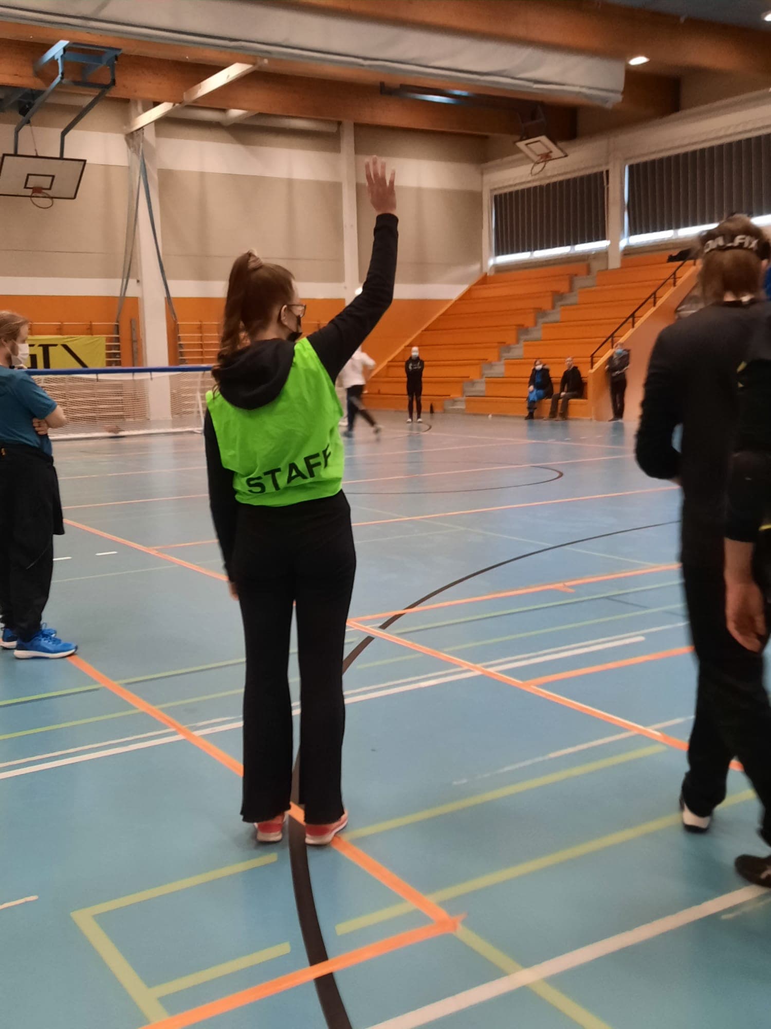 A volunteer woman in a green staff vest has just raised her hand to signal a goal.