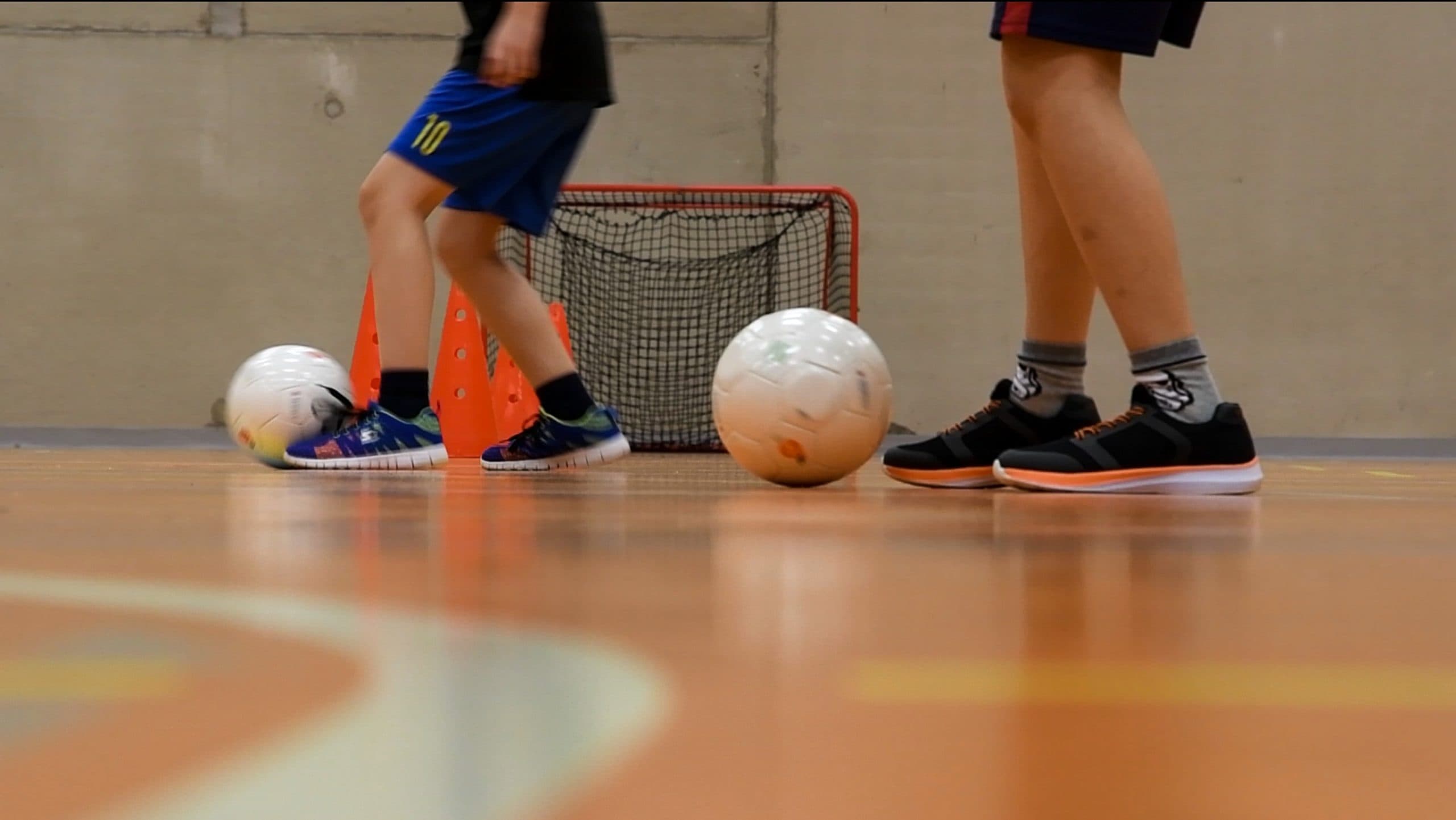 A close-up of two children's legs, the one further back dribbling the ball.