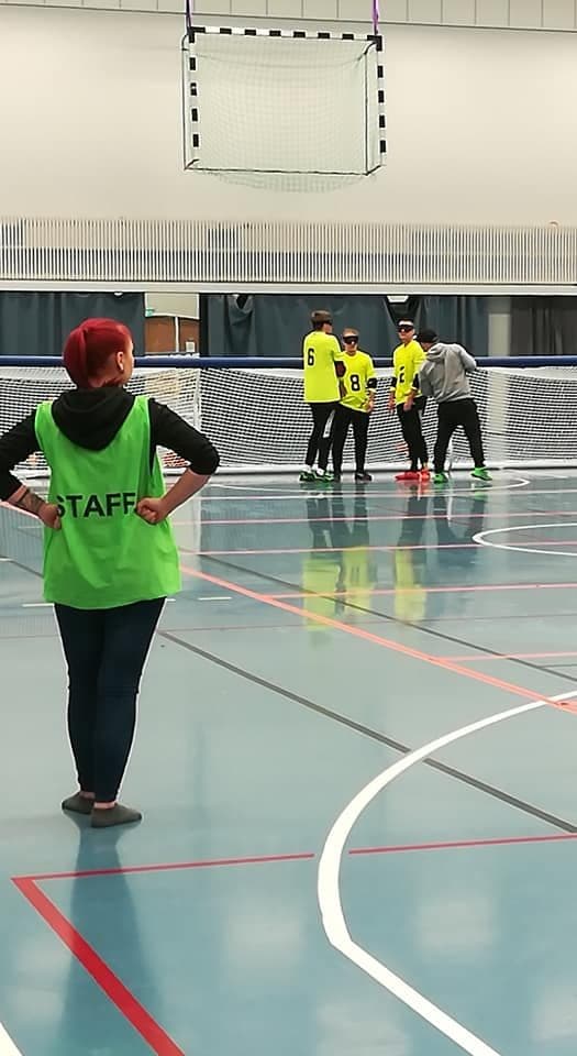 Kuva kotimaisesta turnauksesta, jossa etualalla vapaaehtoinen maalituomari staff-liivi yllään. Taustalla Aistin joukkue aikalisällä.
